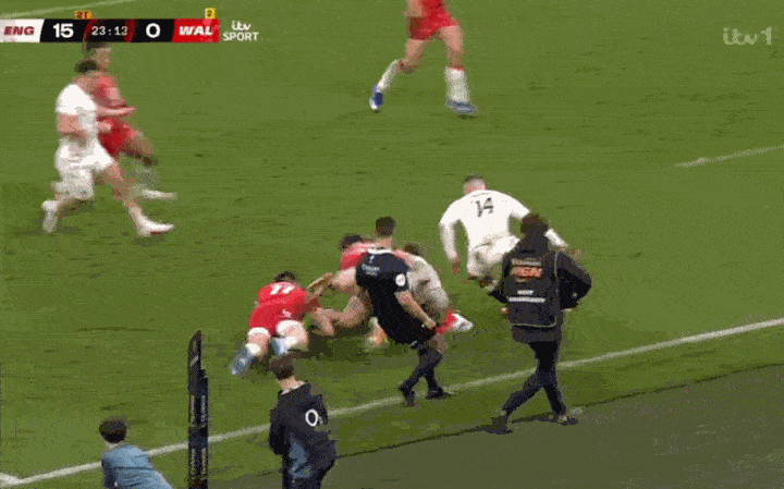 A group of rugby players in white and red jerseys are huddled on the grass during a match between England and Wales.