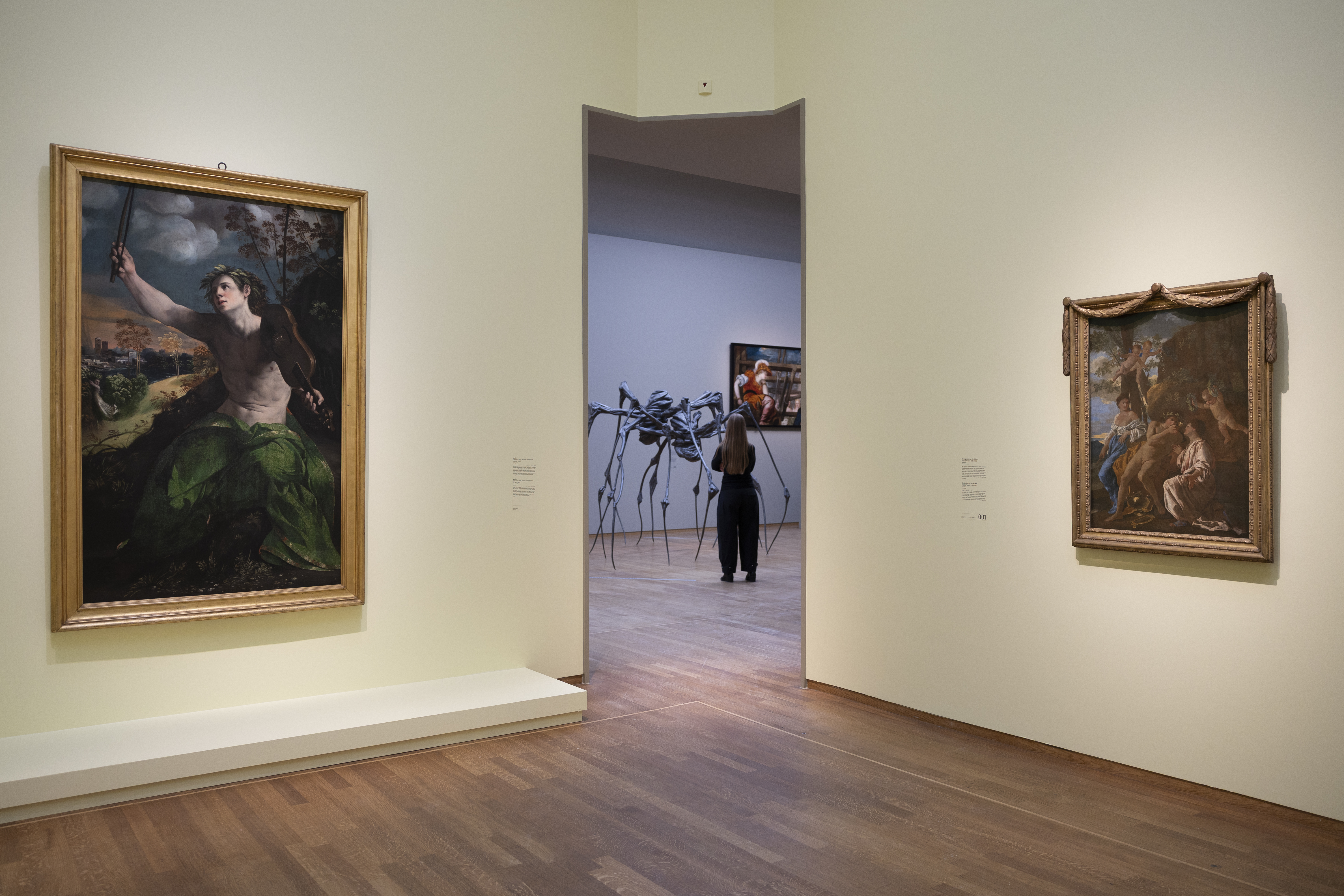 A visitor views "Metamorphoses" exhibition featuring Titian’s "Danaë" and Tintoretto’s "Minerva and Arachne" paintings and a large spider-like sculpture.