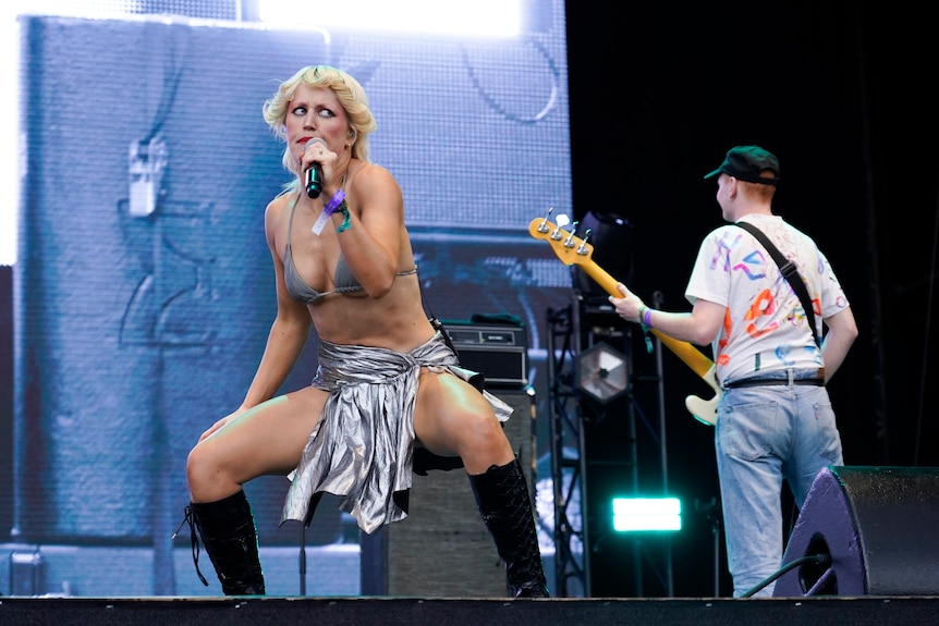 A singer wearing a silver bra and skirt on stage, holing a mic.