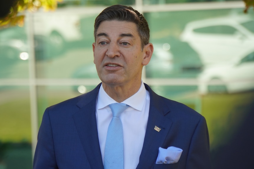 A man in a suit stands outside a window