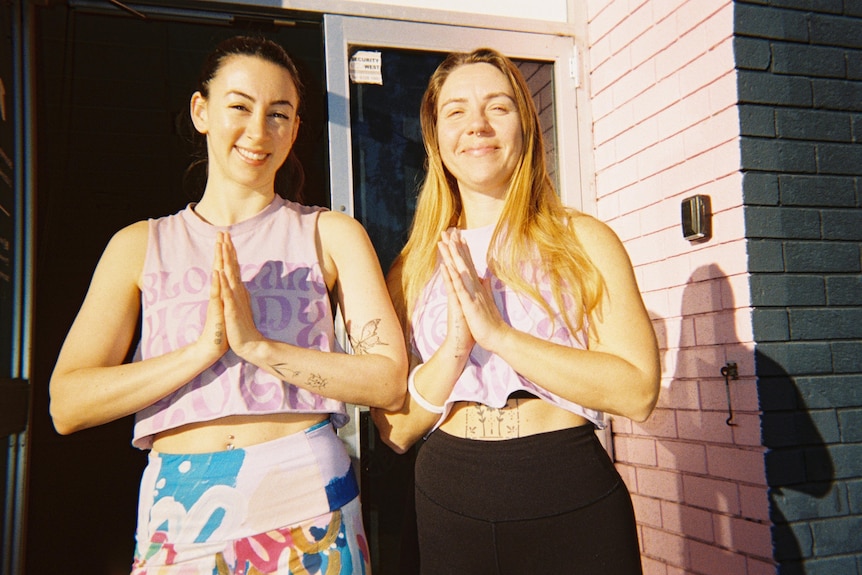 Two girls stand side by side with their hands in prayer position.
