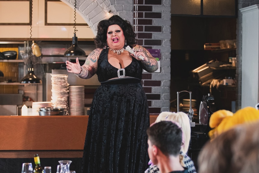 A drag performer dressed in all black performing in front of patrons