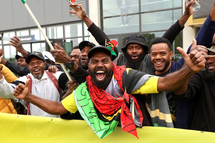A man draped in a Vanuatu flag cheers.