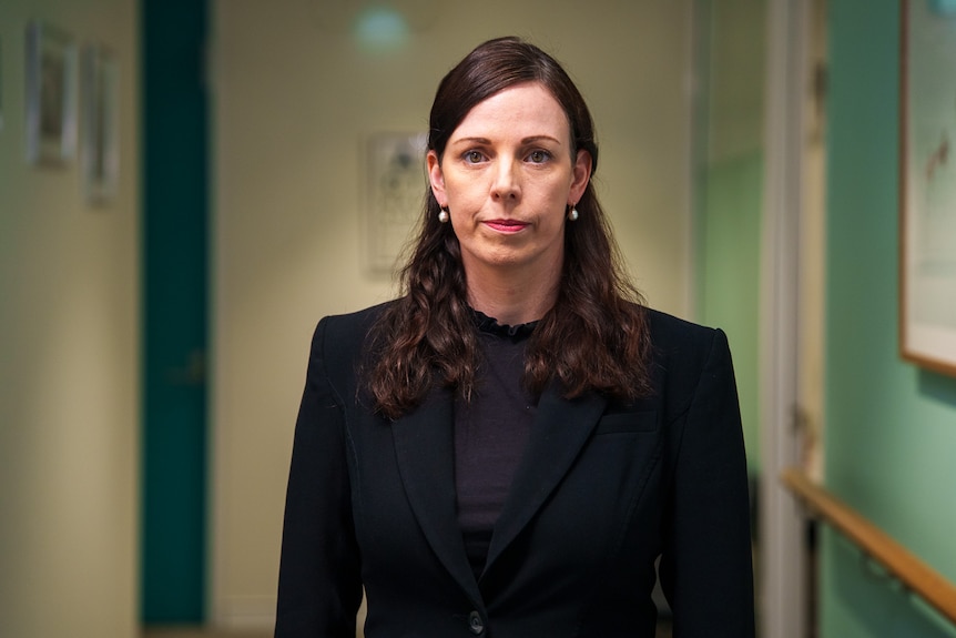 A woman in a black suit, standing in a medical office.