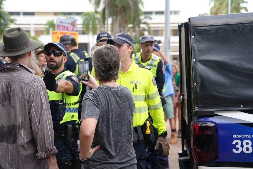 Police officers standing alongside a crowd of protestors.
