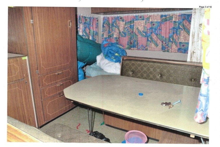 The interior of a caravan. shows a dinner table with a bench seat and a bed in the corner.