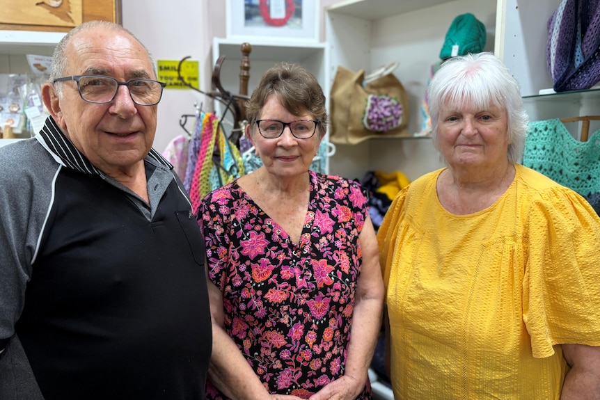 An older man and two older woman stand in a craft centre, smiling.