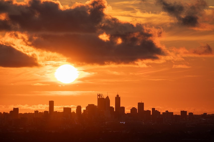 City skyline silhouetted against orange sky as sun sets over Perth.
