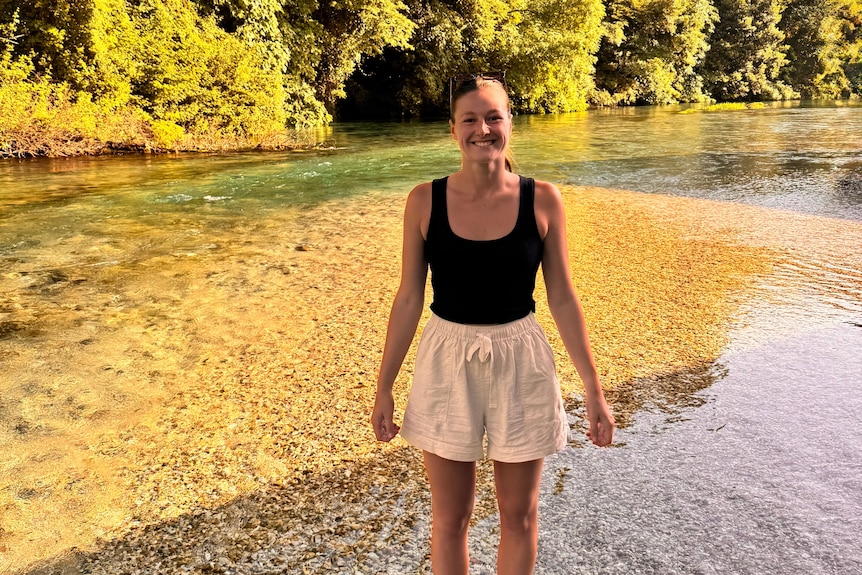 A woman in a black tank top and white shorts smiling while standing in shallow water