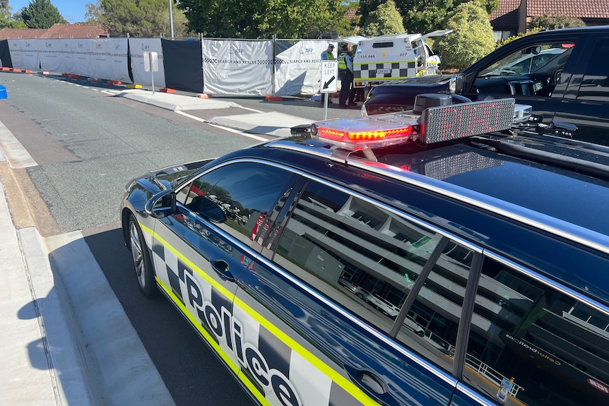 Police car beside white barrier fencing.