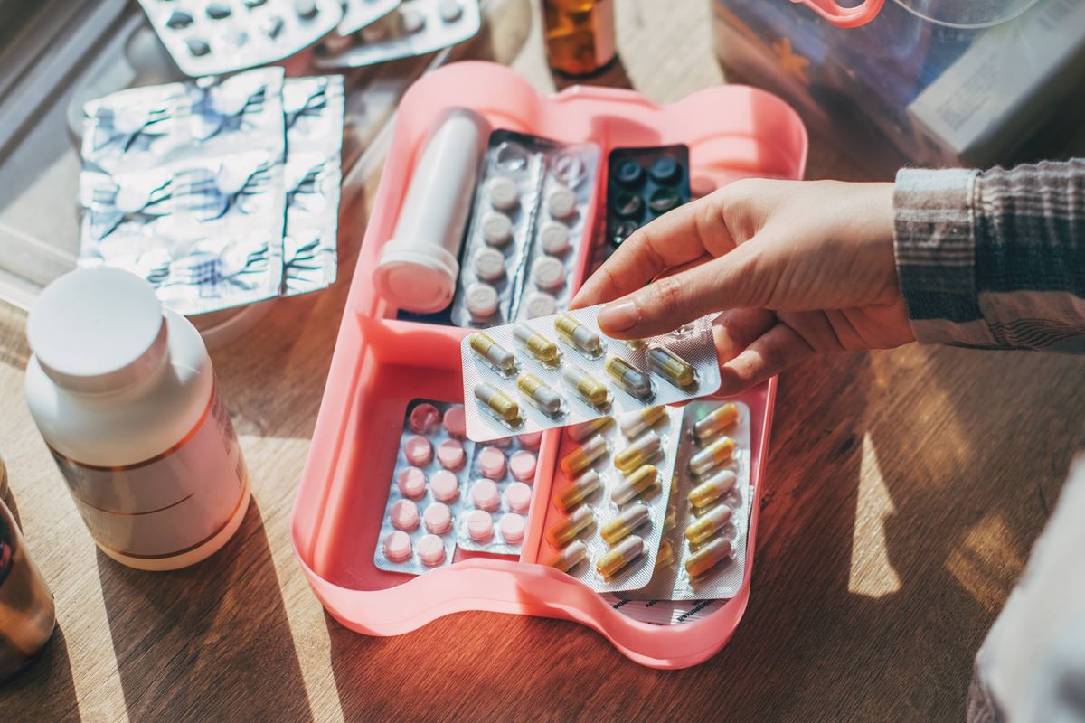 Closeup female hand neatly placing medicament at domestic first aid kit top view. Storage organization in transparent plastic box drug, pill, syringe, bandage. Fast health help safety emergency supply