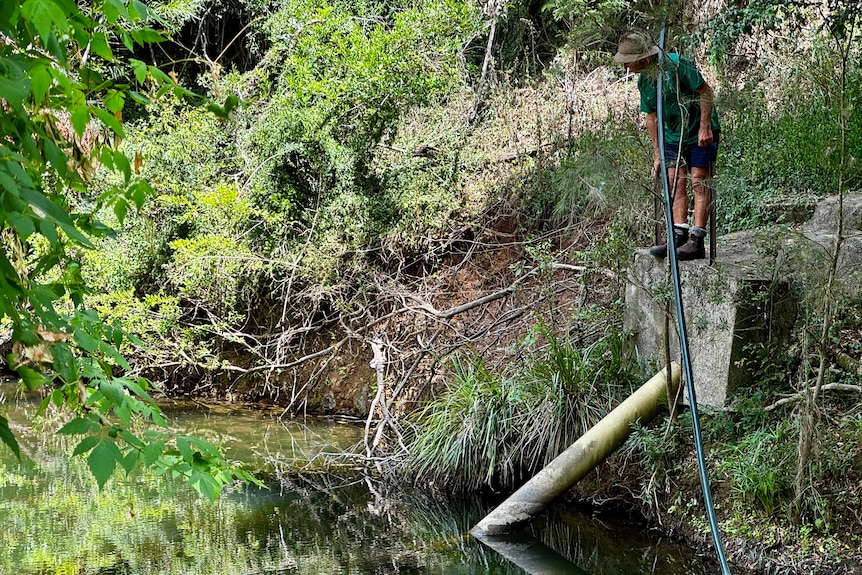 A man looks over a pipe going into a creek.
