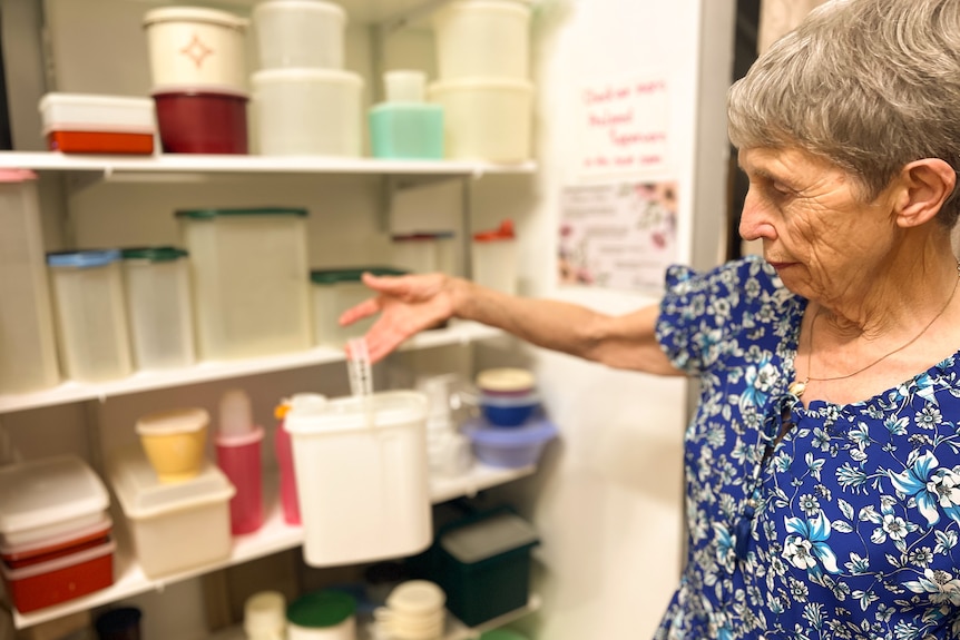 A lady dressed in blue holds a white Tupperware container.