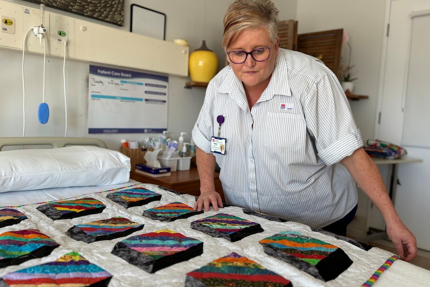 A nurse lays a handmade quilt on a hospital bed.