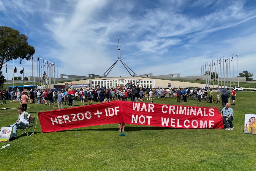A sign at a protest outside Parliament House against Isaac Herzog says "Herzog + IDF war criminals not welcome".