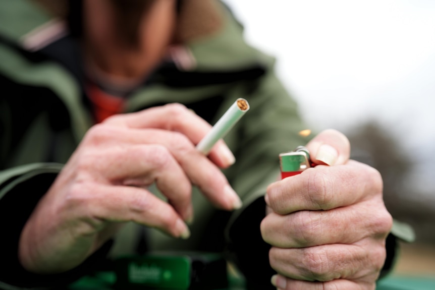 An unidentifiable person's hands holding an unlit cigarette and a lit red lighter.
