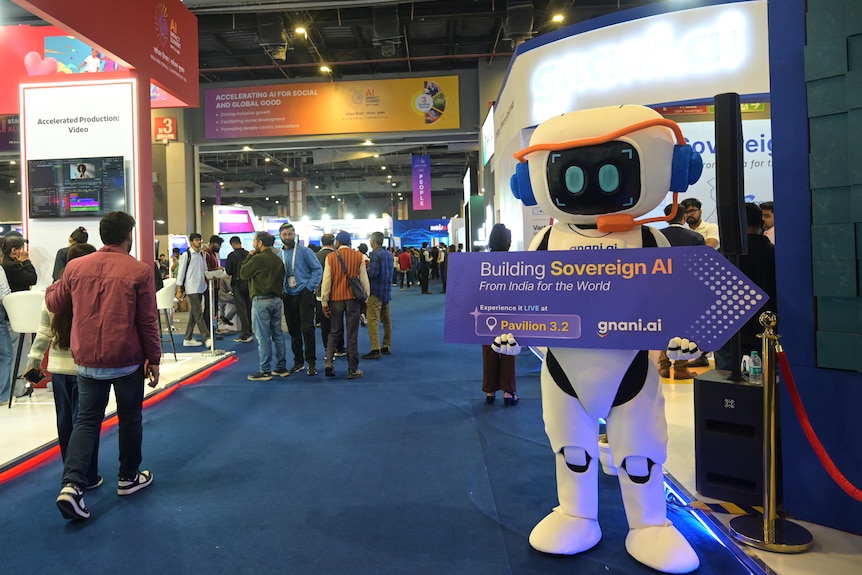 A robot figure holds a sign reading 'building sovereign AI' at a summit in New Delhi