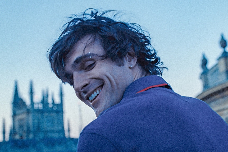 Young man  smiles at camera with mansion in background
