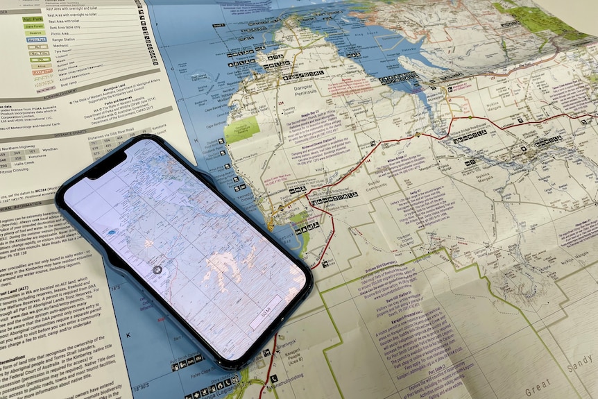A paper map spread on a table with a mobile phone map app open.