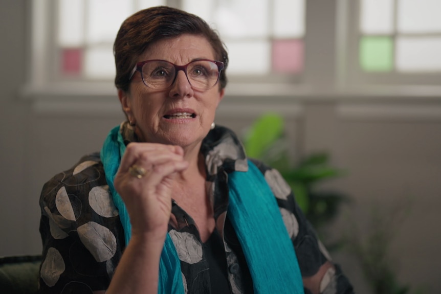 A woman with short hair and glasses talking expressively