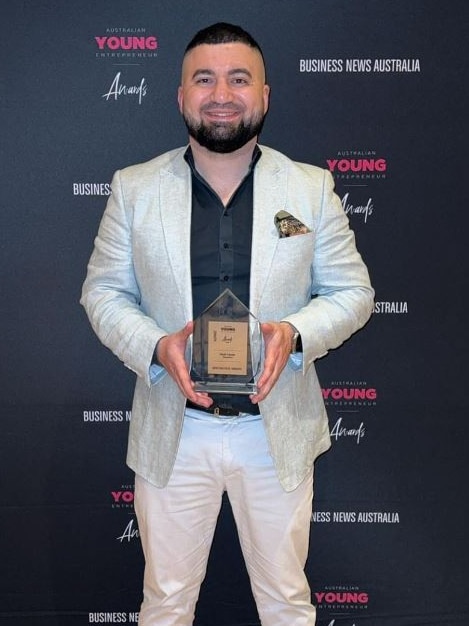 A man smiles and holds an award