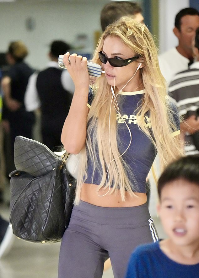 The blonde failed to raise a smile as she clutched her phone and dragged her designer suitcase behind her