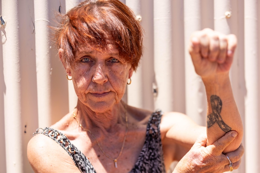 A woman pointing to a tattoo on her left arm.  