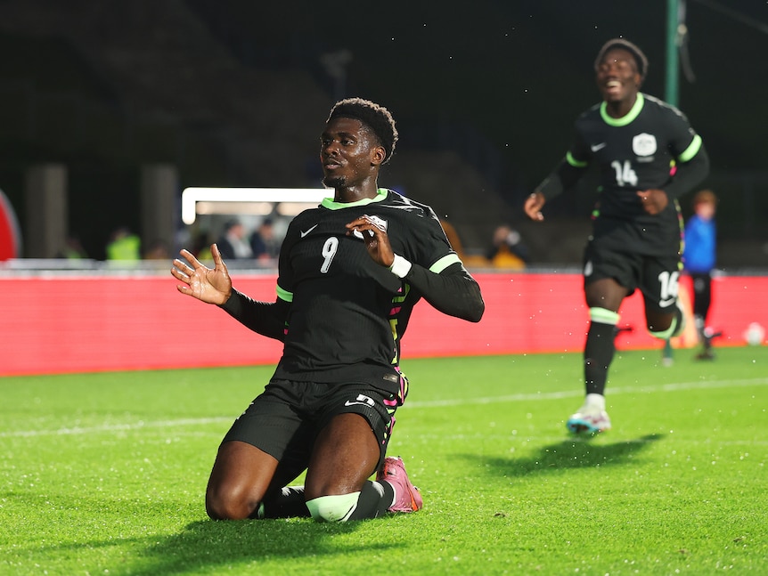 An Australian soccer player slides on his knees in celebration after scoring a goal.