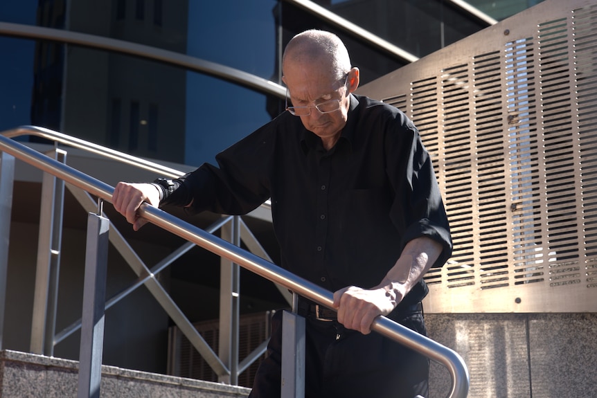 A man holds onto the railing of stairs leading down from a building.