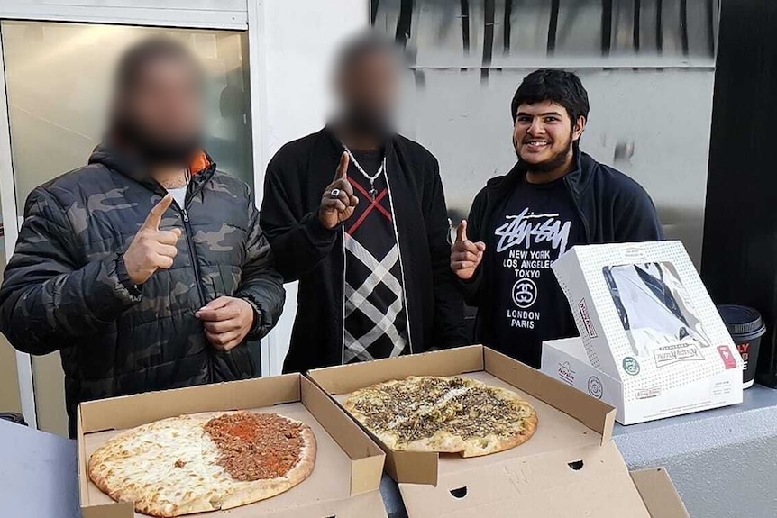 Naveed Akram and two men with blurred faces stand smiling and making a gesture with their index fingers.