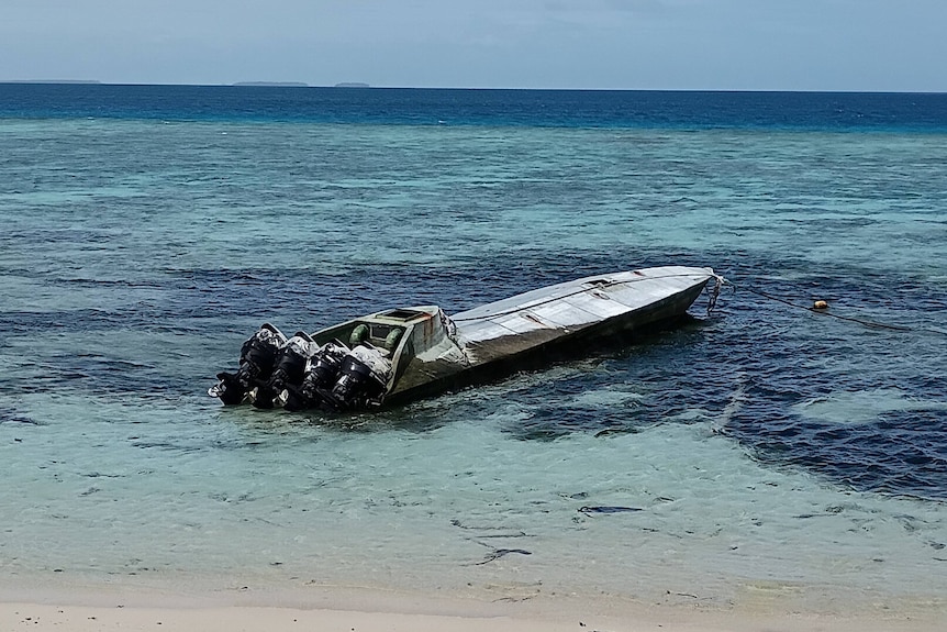 A long grey semi-submersible vessel with four motors ashore at a beach.