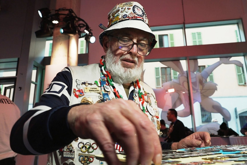 A man wearing a vest and a hat covered in Olympic pins