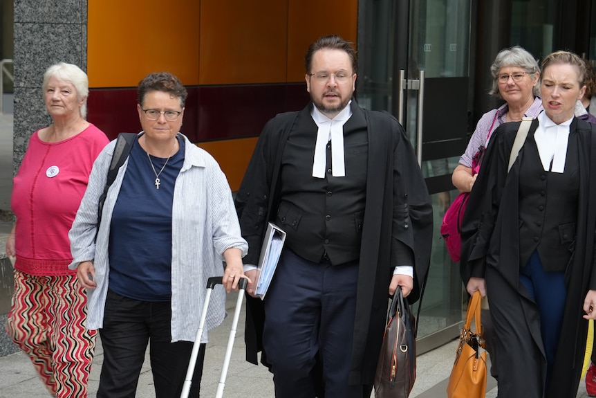 Two lawyers walk away from a court building, surrounded by a group of women