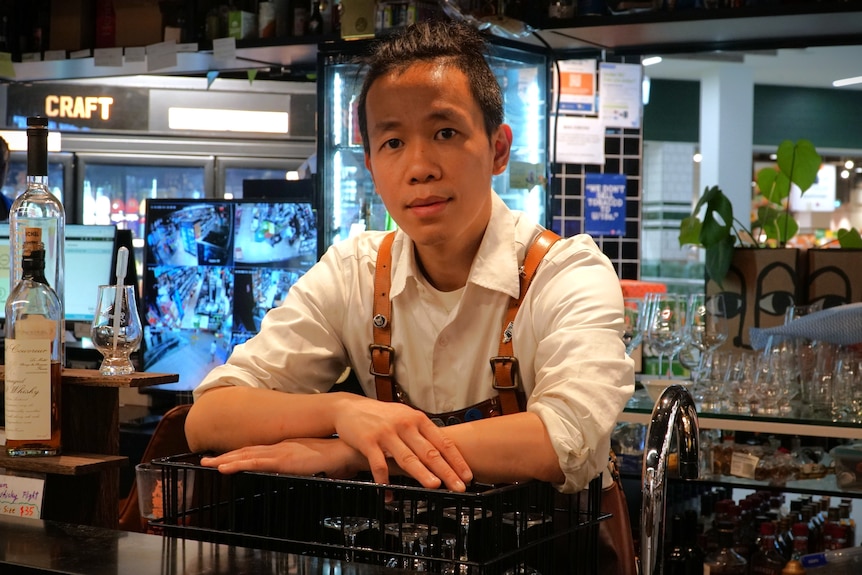 A man in an apron leans over the counter of a bar