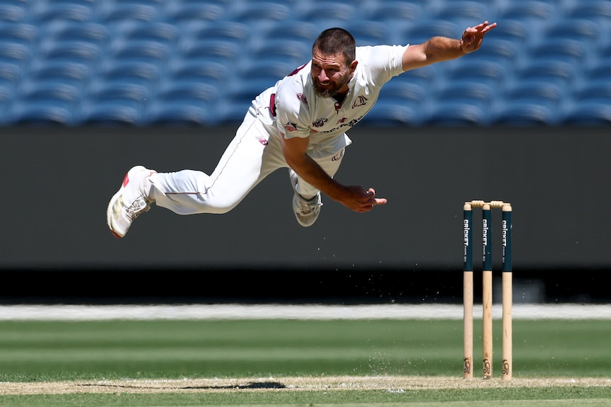 Queensland bowler Michael Neser in the air after bowling a ball.