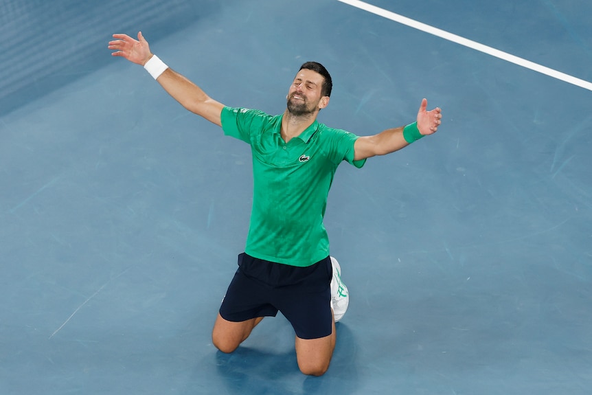 Novak Djokovic on his knees puts his arms out after beating Jannik Sinner in their Australian Open semifinal.