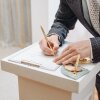 A young man standing at wedding ceremony and signing wedding documents, groom in black costume, cropped, unrecognizable.