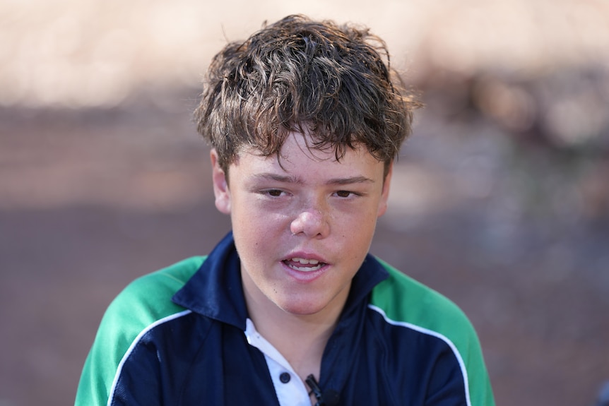 A close-up shot of a boy with short brown hair, wearing his school uniform shirt, speaking during a media interview.