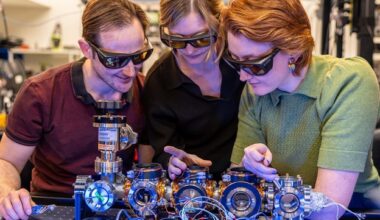 Three people wearing protective glasses, standing next to equipment associated with optical atomic clocks