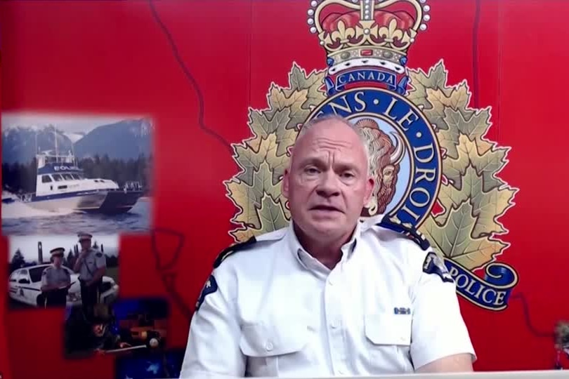 a police officer speaks in front of a red background in a press conference