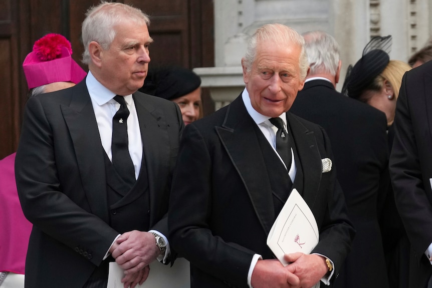 King Charles and Andrew Mountbatten Windsor in black suits and ties, as the King holds a paper booklet.