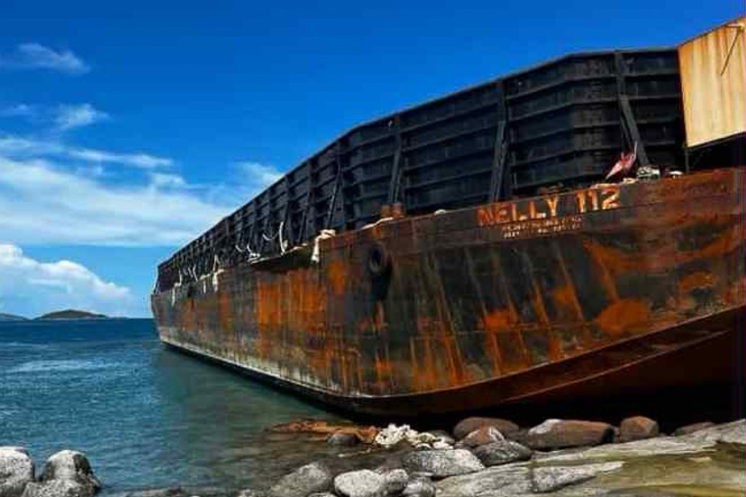 Large vessel with the name Nelly 112 on the hull stranded on rocks surrounded by water