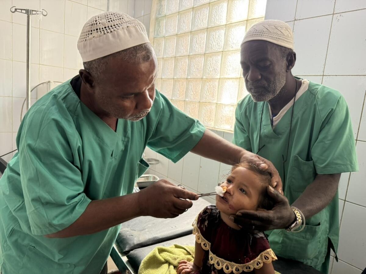 Two people in green shirts hold a child's head.
