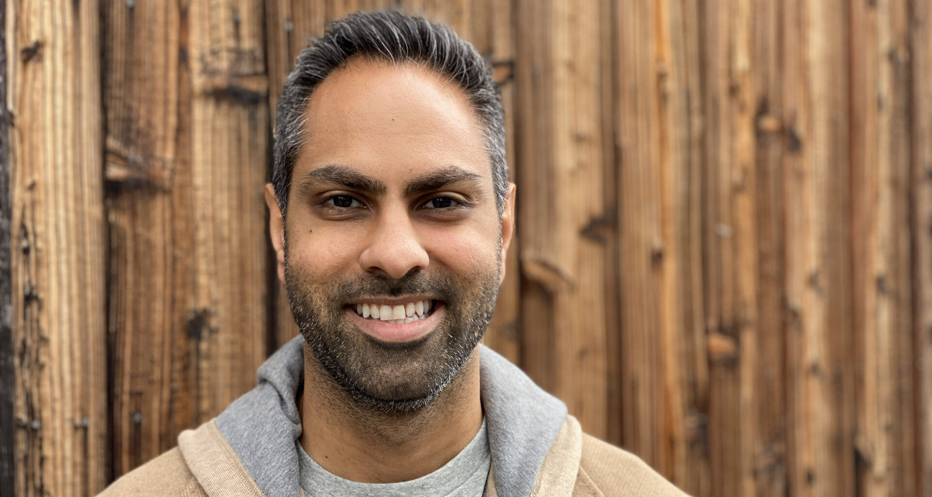 Ramit Sethi smiling with a wooden wall in the background.