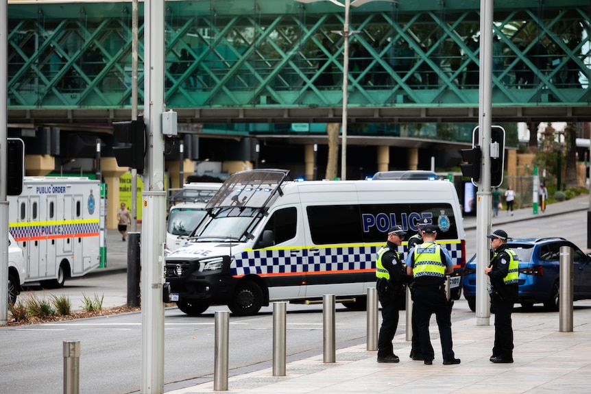 Three police officers talking in front of police vehicles parked across a street.