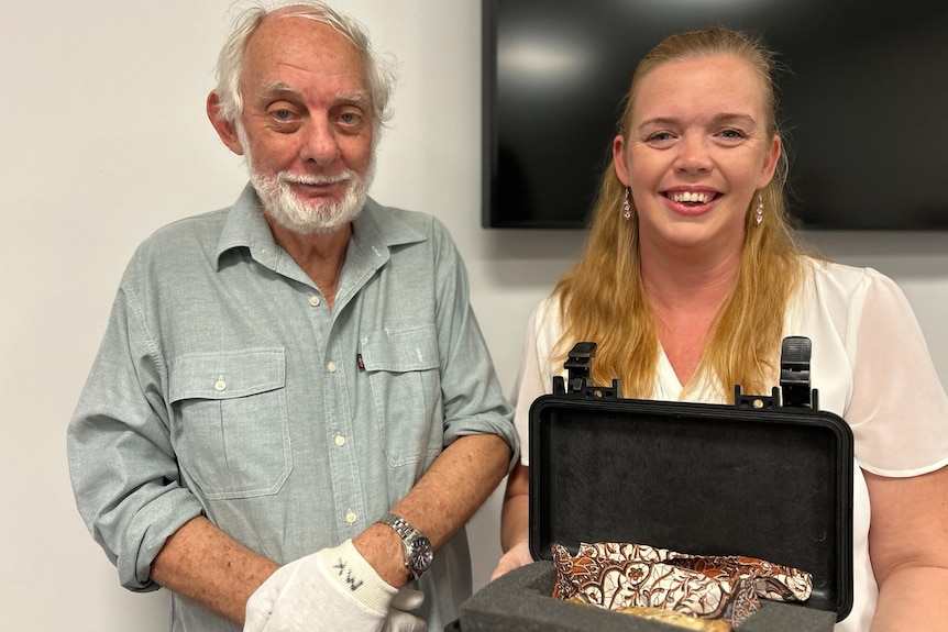 A man and a woman hold a briefcase which contains a cat statue