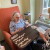 Rita Orr, 94, and her daughter Janice Rogers are pictured sitting across a small table from each other, with game tiles and cards arrayed in front of them.