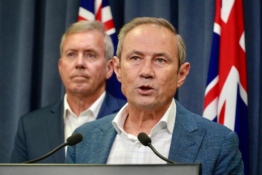 A man speaks in front of an Australian flag.