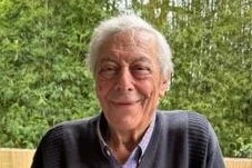 A smiling, older man sitting in a garden.