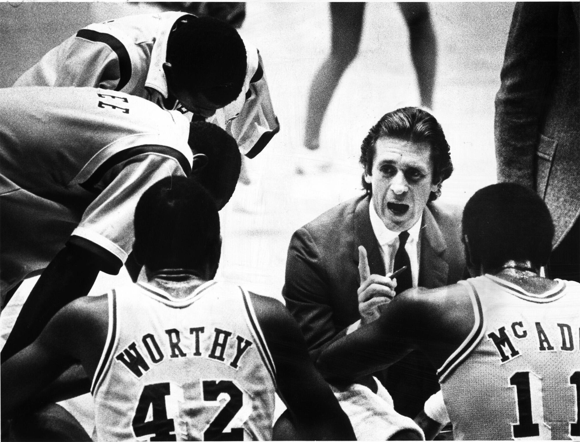 Lakers coach Pat Riley takes a knee as he talks to his players on the bench, including James Worthy and Bob McAdoo.